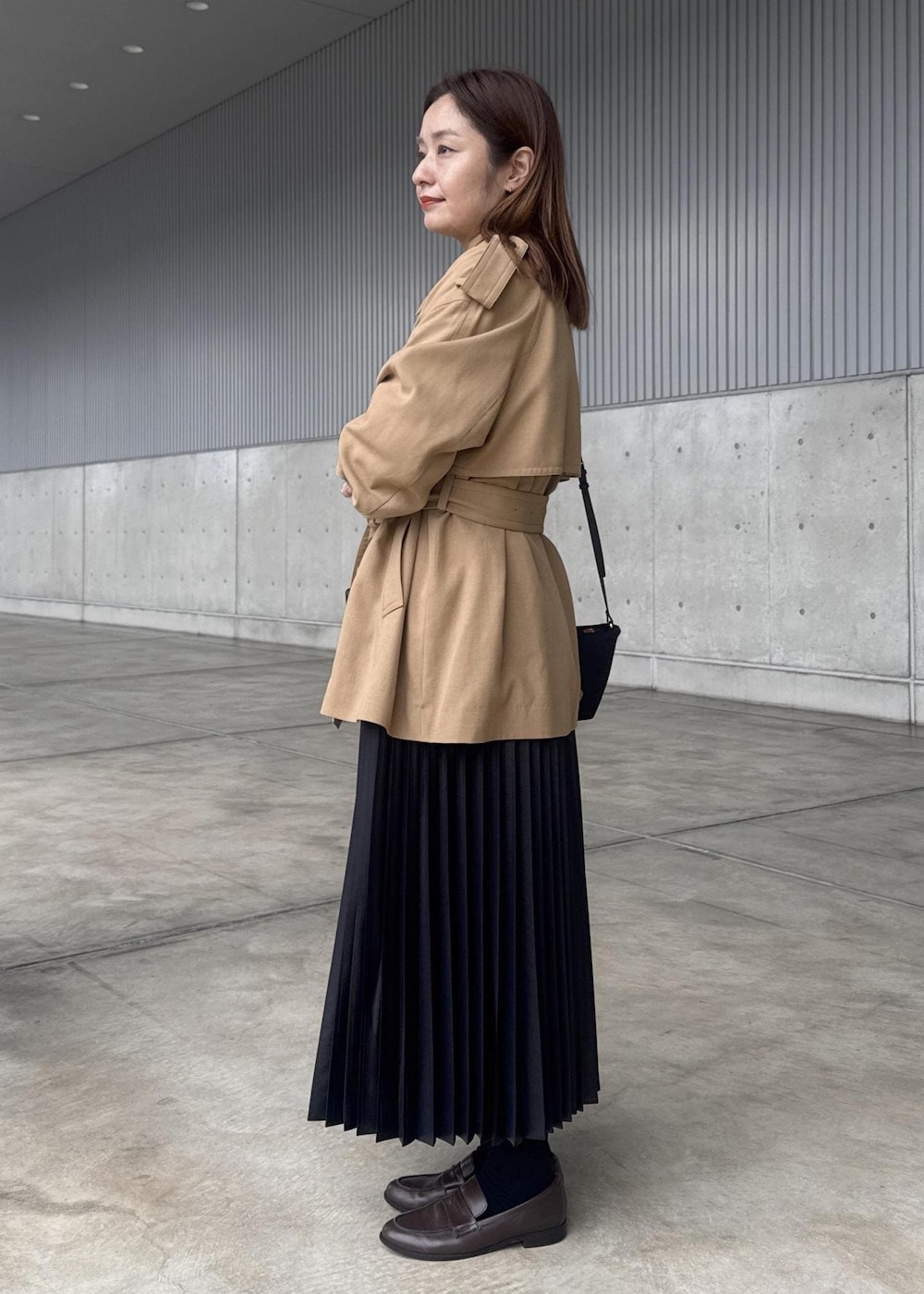 ブラック系のスカート、ブラック系のショルダーバッグ、ベージュ系のトレンチコートを着用したレディースの春コーディネートの7枚目の写真