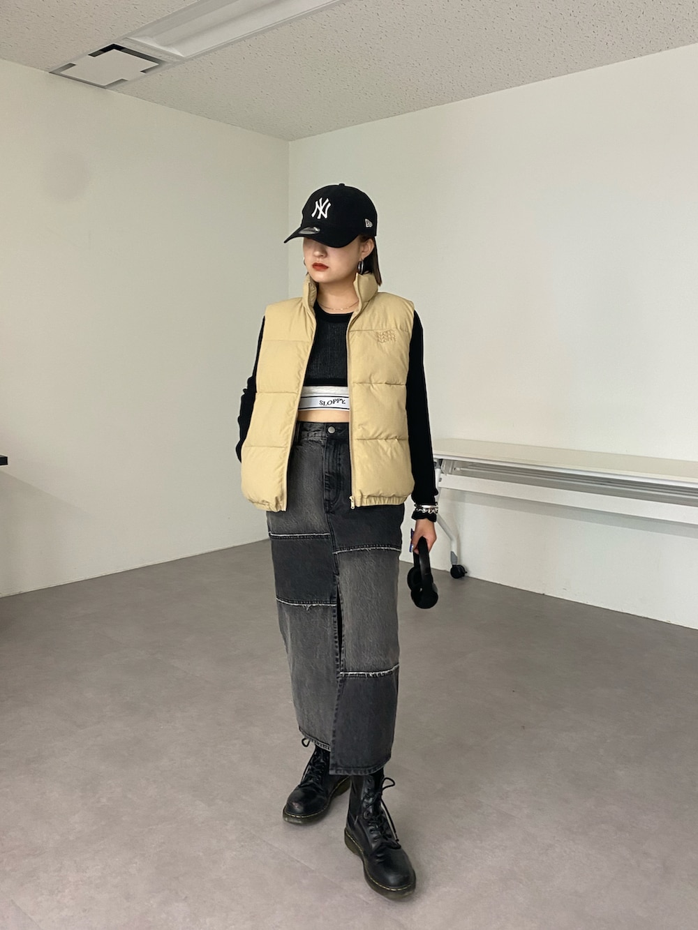 ブラック系のデニムスカート、ベージュ系のダウンベスト、ブラック系のTシャツ/カットソーを着用したレディースの秋コーディネートの2枚目の写真