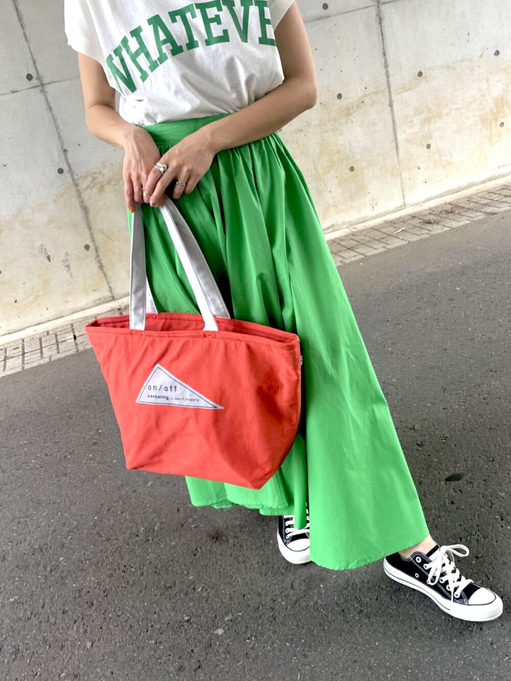 グリーン系のスカート、オレンジ系のトートバッグ、ブラック系のスニーカーを着用したレディースの夏コーディネートの3枚目の写真