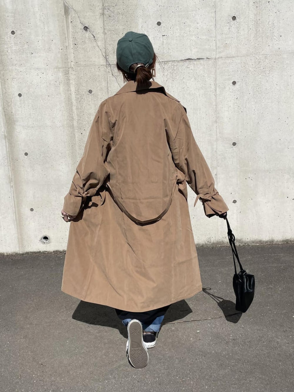 ブラック系のワンピース、ブラウン系のトレンチコート、ブラック系のショルダーバッグを着用したレディースの春コーディネートの2枚目の写真