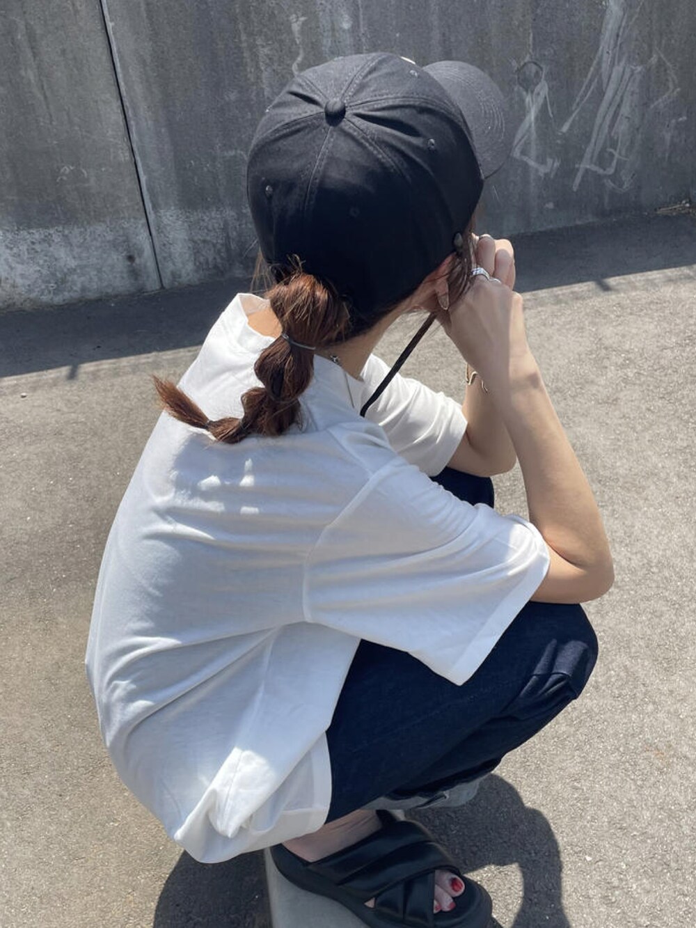 ブルー系のデニムパンツ、ブラック系のサンダル、ホワイト系のTシャツ/カットソーを着用したレディースの夏コーディネートの2枚目の写真