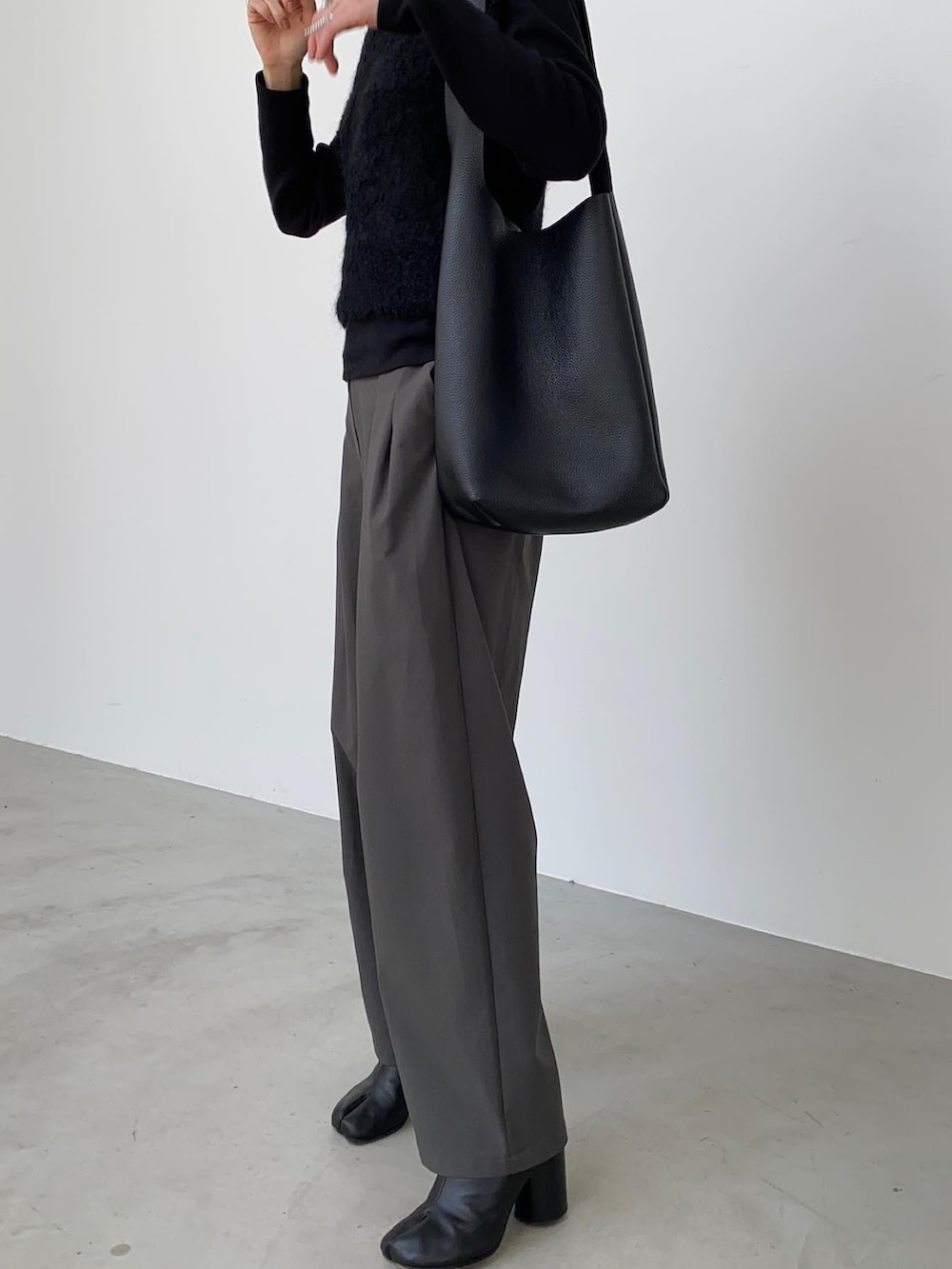 グレー系のスラックス、ブラック系のトートバッグ、ブラック系のブーツを着用したレディースの秋コーディネートの2枚目の写真