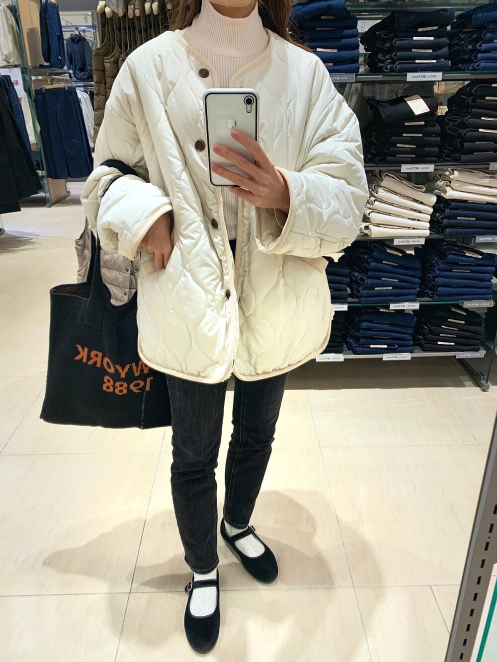 ホワイト系のノーカラージャケット、ブルー系のデニムパンツ、ブラック系のトートバッグを着用したレディースの冬コーディネートの2枚目の写真