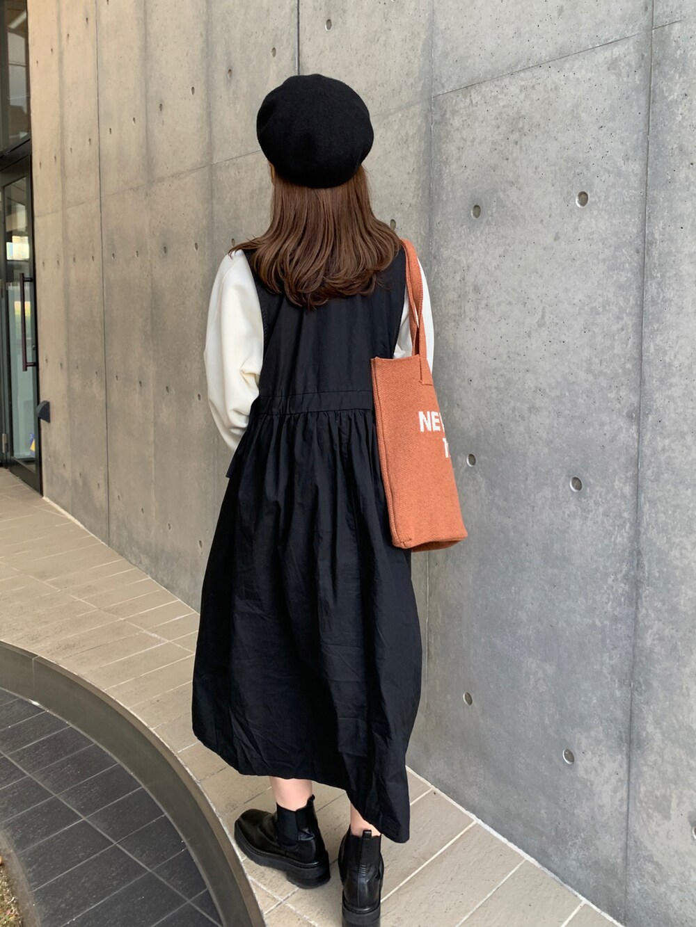 ホワイト系のスウェット、ブラック系のジャンパースカート、ブラウン系のトートバッグを着用したレディースの冬コーディネートの2枚目の写真