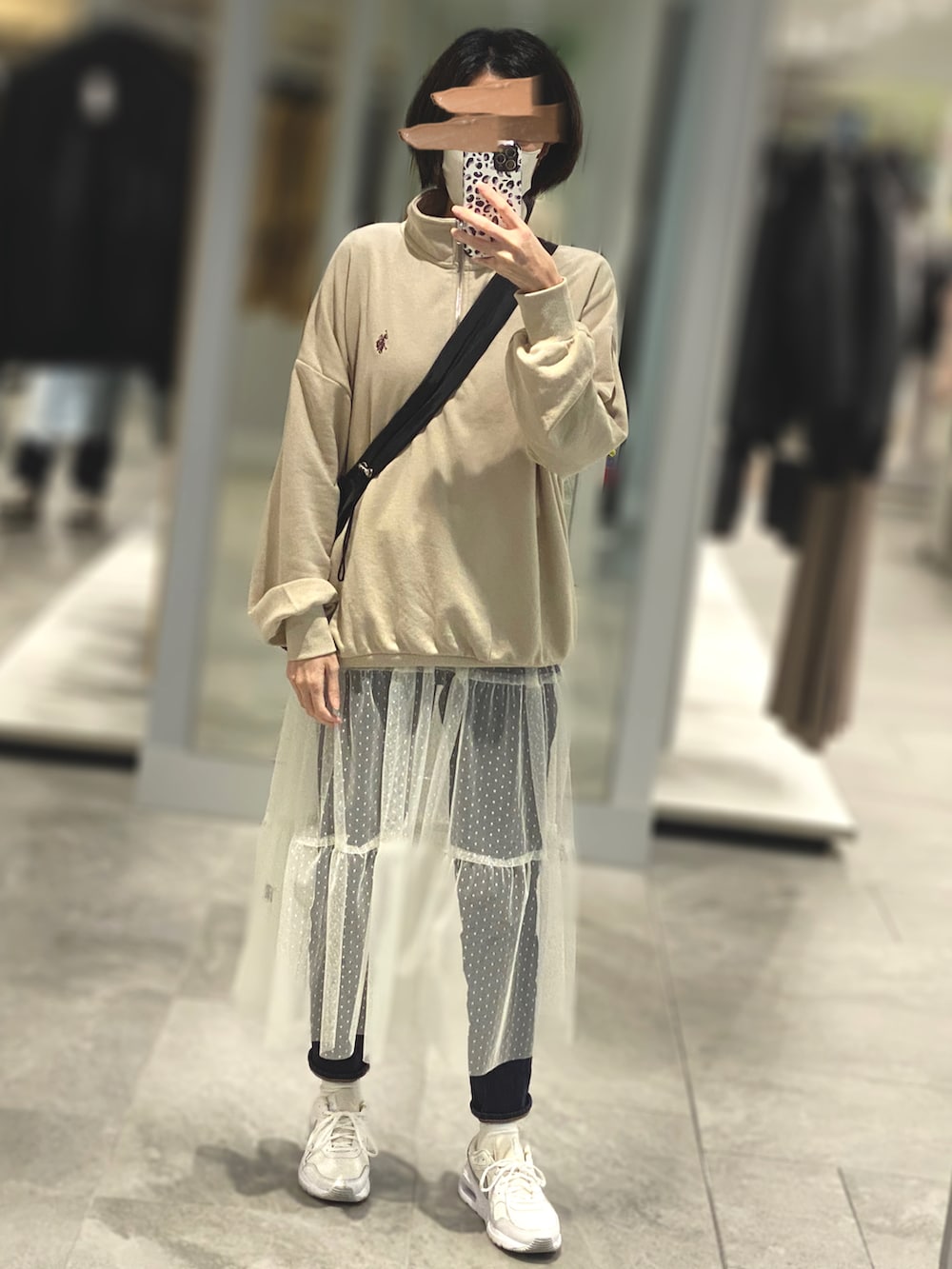 ベージュ系のスウェット、ホワイト系のワンピース、ブラック系のデニムパンツを着用したレディースの春コーディネートの2枚目の写真
