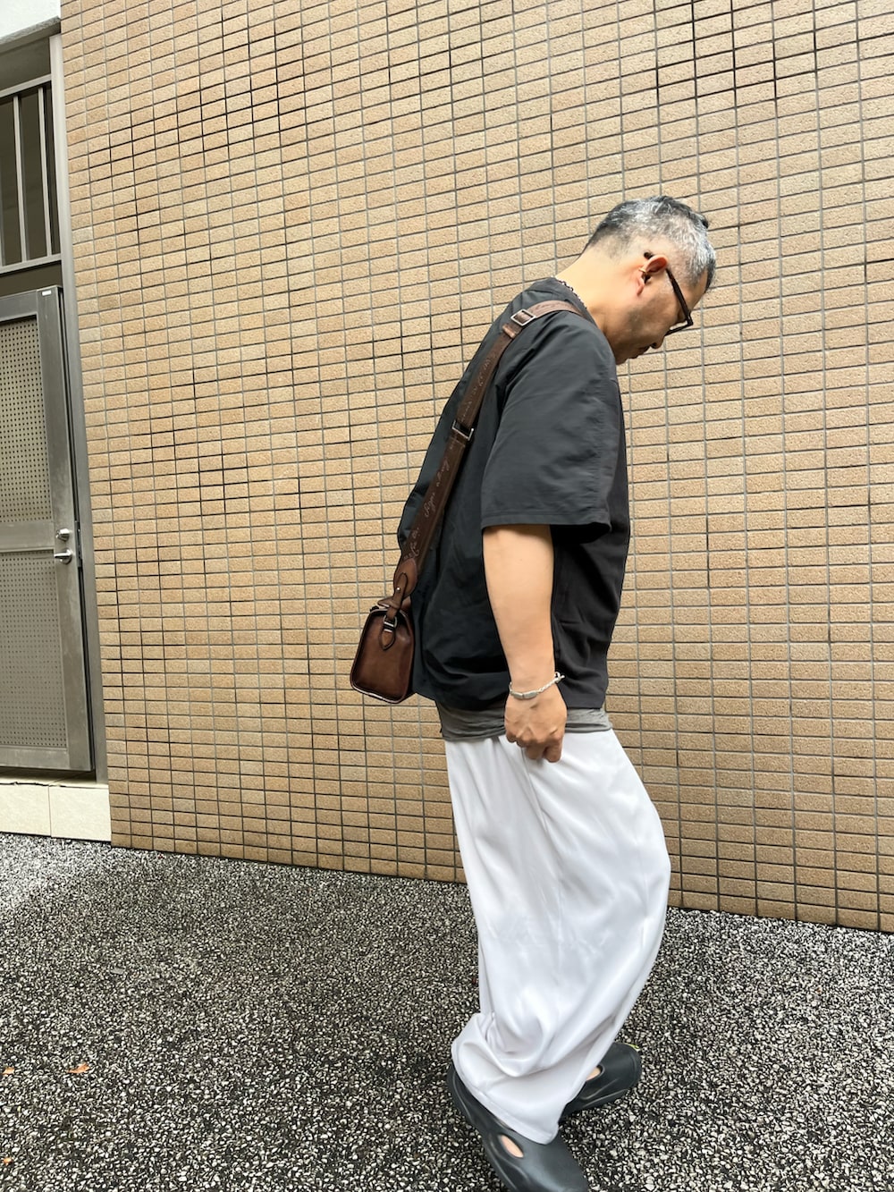 ブラック系のTシャツ/カットソー、ブラウン系のボディバッグ/ウエストポーチ、ホワイト系のスラックスを着用したメンズの夏コーディネートの2枚目の写真