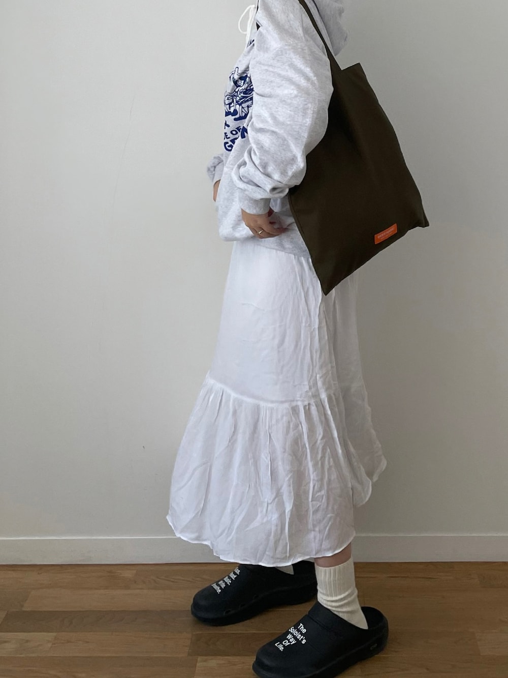 ホワイト系のスカート、グリーン系のトートバッグ、ブラック系のキャップを着用したレディースの秋コーディネートの2枚目の写真