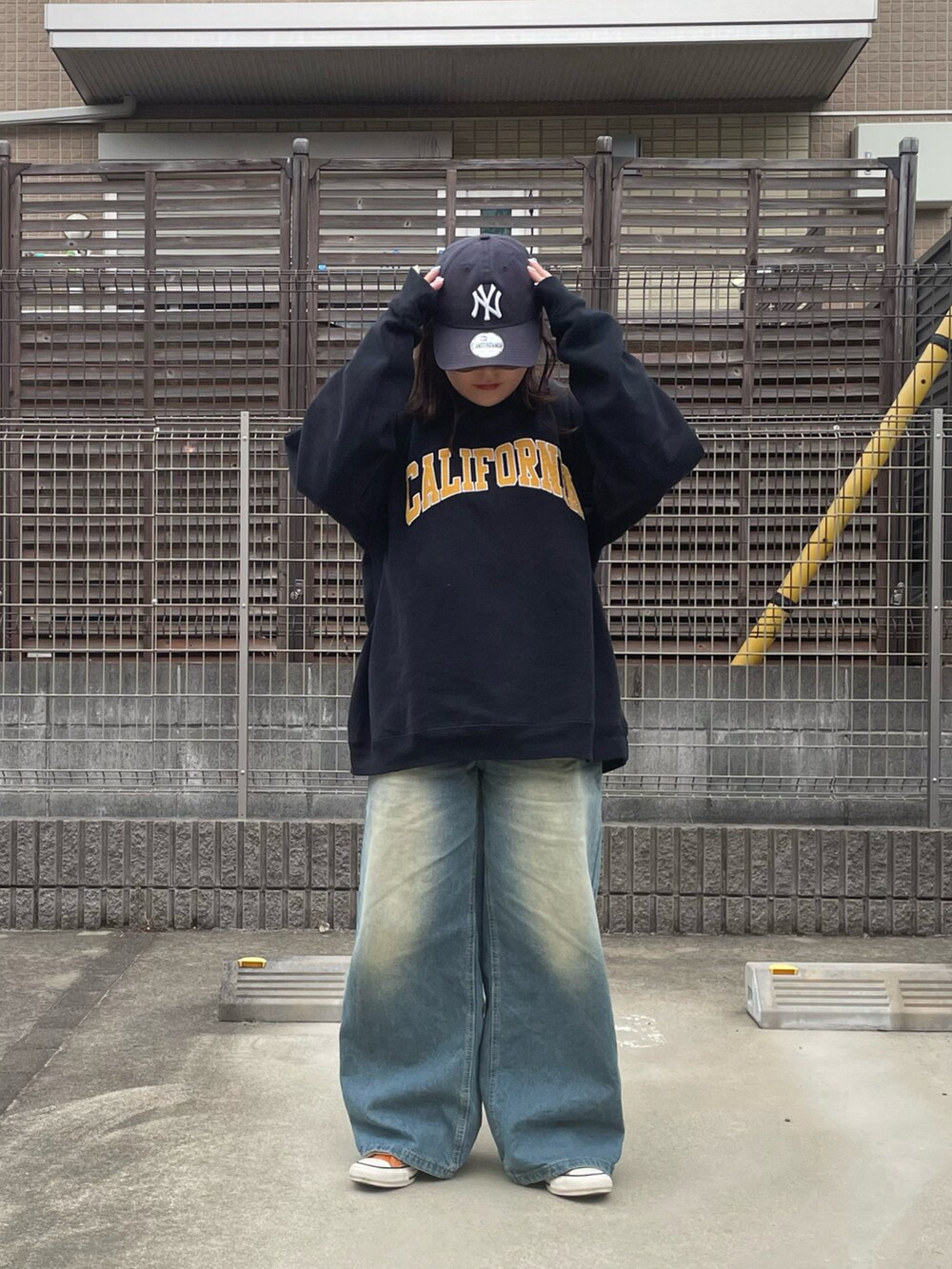 ブラック系のスウェット、オレンジ系のスニーカー、ブルー系のデニムパンツを着用したレディースの春コーディネートの2枚目の写真