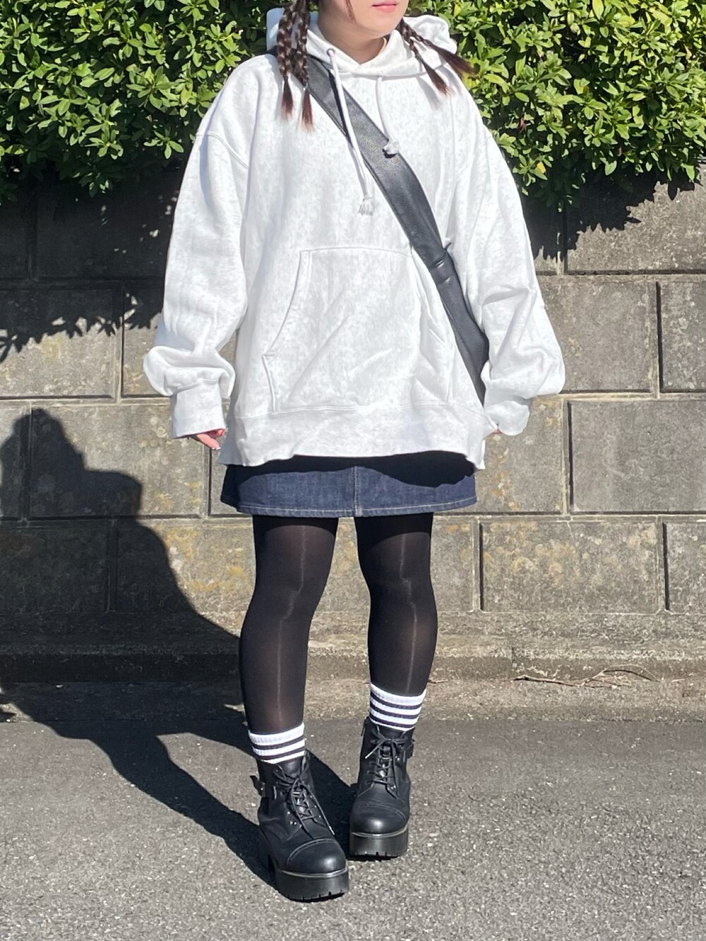 ブラック系のショルダーバッグ、ブルー系のデニムスカート、ブラック系のブーツを着用したレディースの冬コーディネートの2枚目の写真