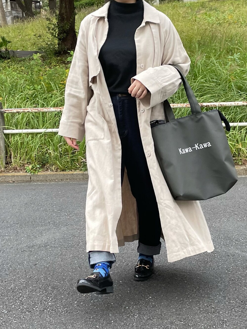 ホワイト系のステンカラーコート、ブルー系のデニムパンツ、グリーン系のトートバッグを着用したレディースの秋コーディネートの2枚目の写真