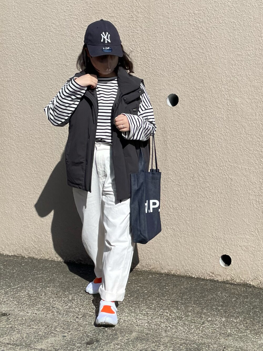 ブラック系のダウンベスト、ブルー系のトートバッグ、ホワイト系のパンツを着用したレディースの春コーディネートの2枚目の写真