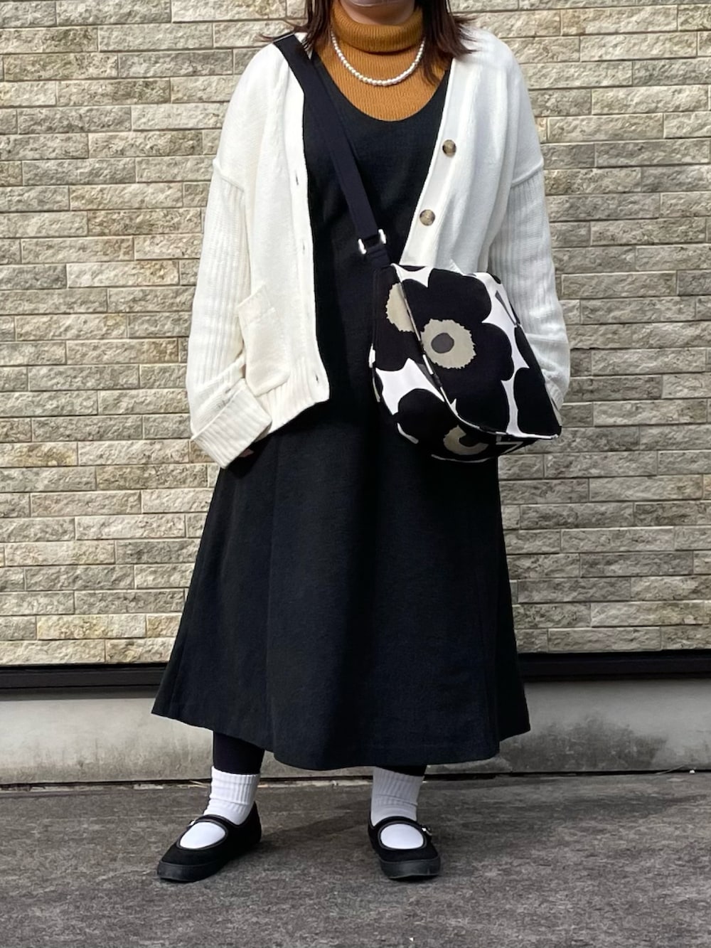 ブラック系のブルゾン、イエロー系のニット/セーター、ブラック系のジャンパースカートを着用したレディースの冬コーディネートの2枚目の写真