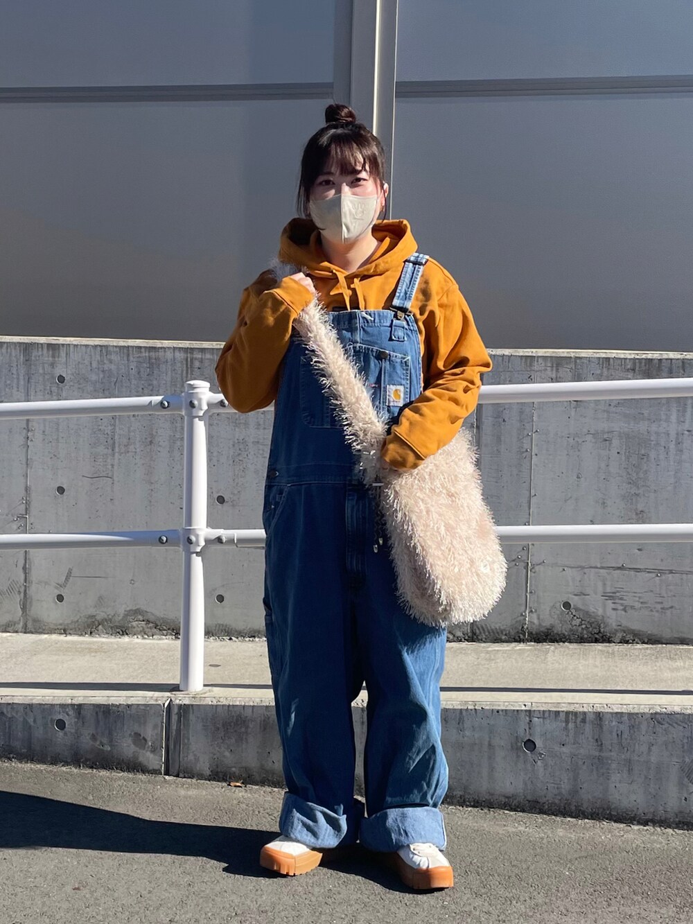 ベージュ系のショルダーバッグ、ブルー系のサロペット/オーバーオール、ホワイト系のスニーカーを着用したレディースの冬コーディネートの2枚目の写真