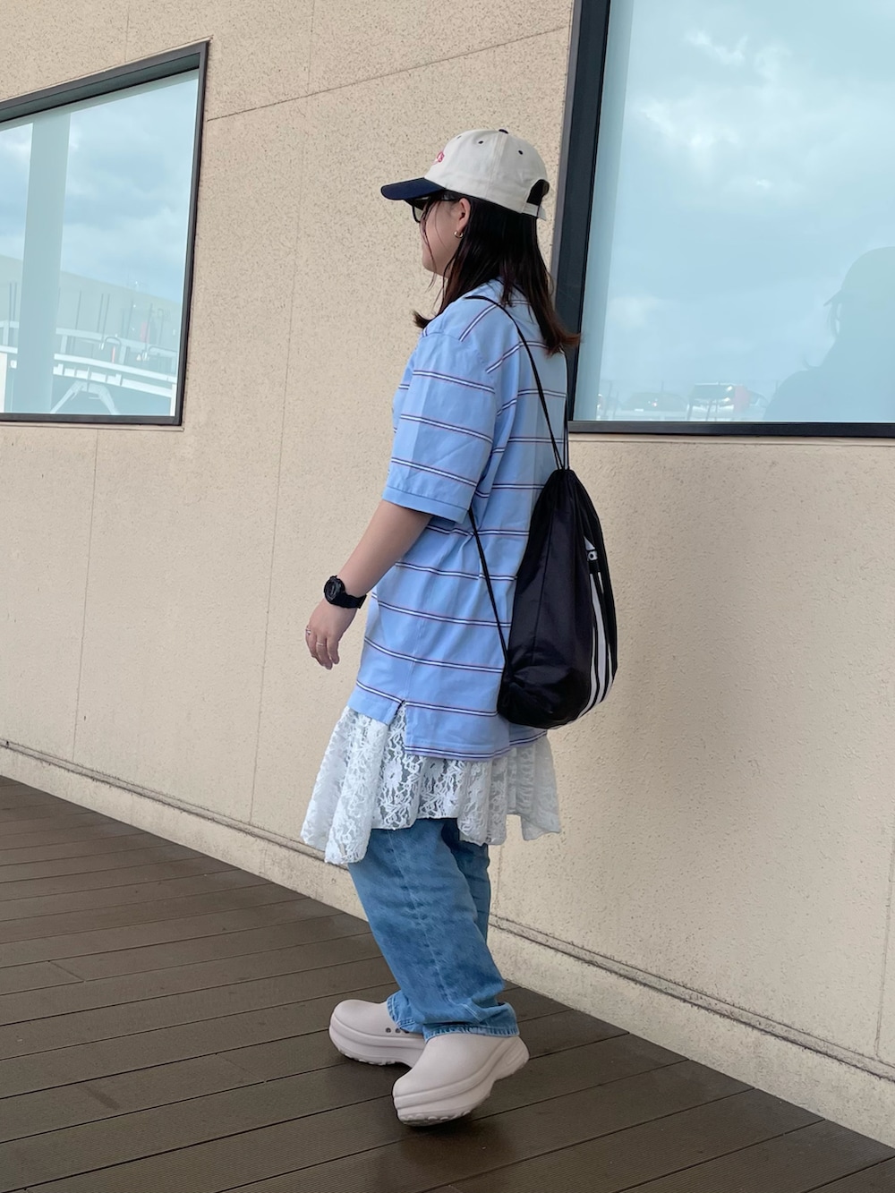 ブルー系のポロシャツ、ベージュ系のサンダル、ブラック系のバックパック/リュックを着用したレディースの夏コーディネートの2枚目の写真