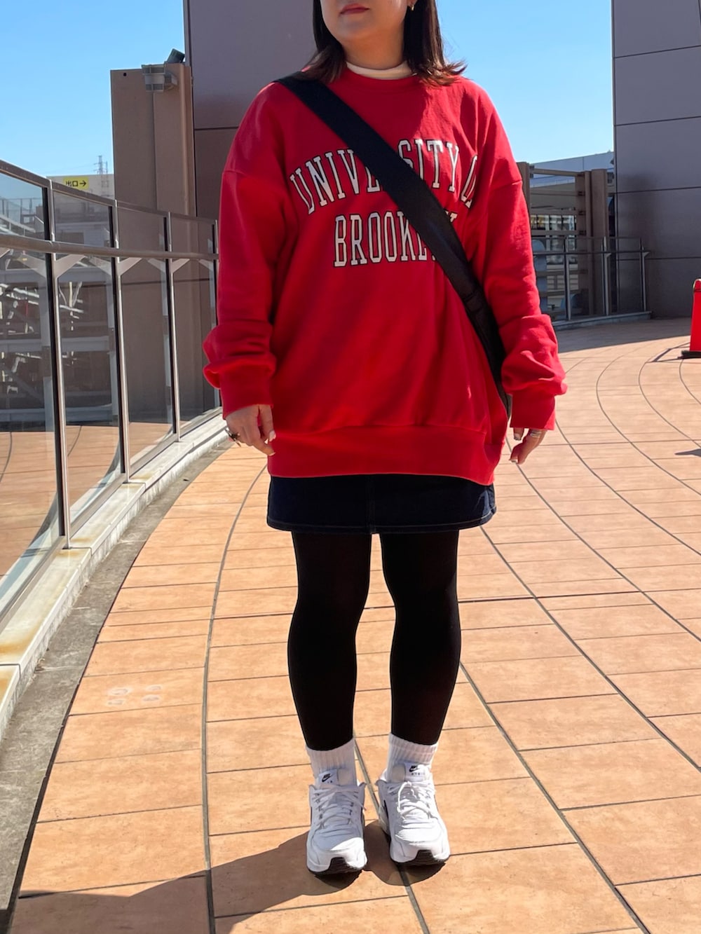 ブラック系のショルダーバッグ、レッド系のスウェット、ブルー系のデニムスカートを着用したレディースの春コーディネートの2枚目の写真