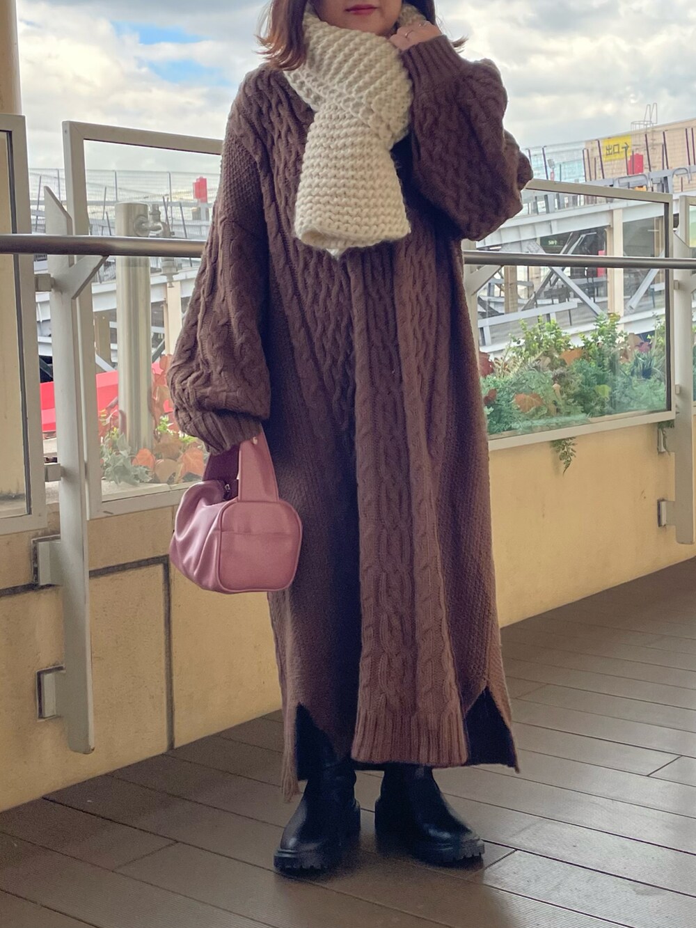 ブラウン系のワンピース、ピンク系のボストンバッグ、ブラック系のブーツを着用したレディースの冬コーディネートの2枚目の写真