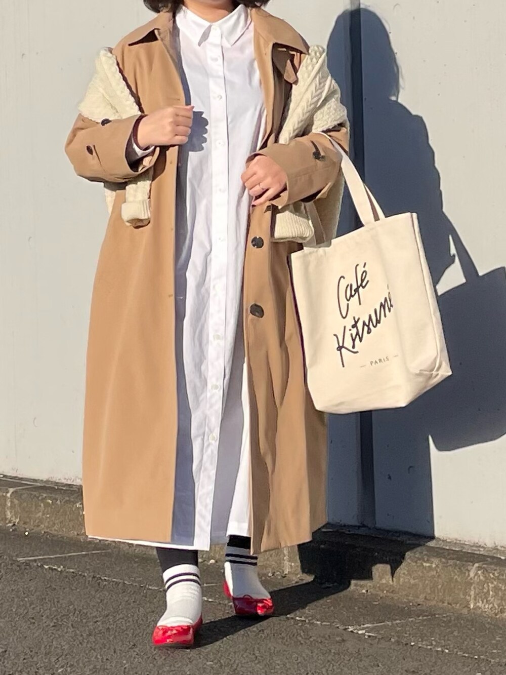 ベージュ系のステンカラーコート、ホワイト系のシャツワンピース、ホワイト系のトートバッグを着用したレディースの春コーディネートの2枚目の写真