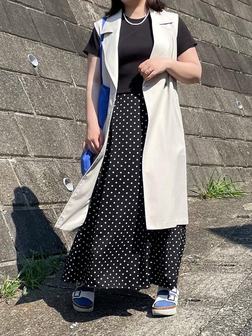 ブラック系のスカート、ホワイト系のサンダル、ブルー系のトートバッグを着用したレディースの春コーディネートの2枚目の写真