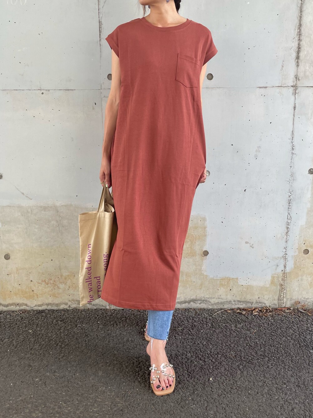 オレンジ系のワンピース、ベージュ系のトートバッグ、ブルー系のデニムパンツを着用したレディースの夏コーディネートの2枚目の写真