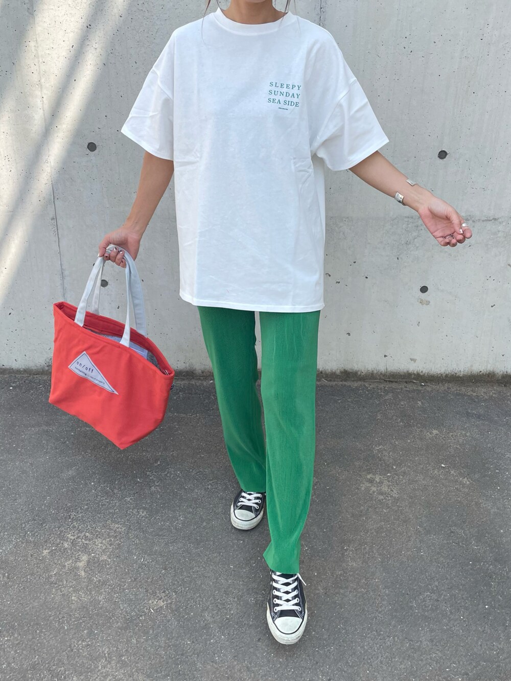 グリーン系のTシャツ/カットソー、オレンジ系のトートバッグ、ブラック系のスニーカーを着用したレディースの春コーディネートの2枚目の写真
