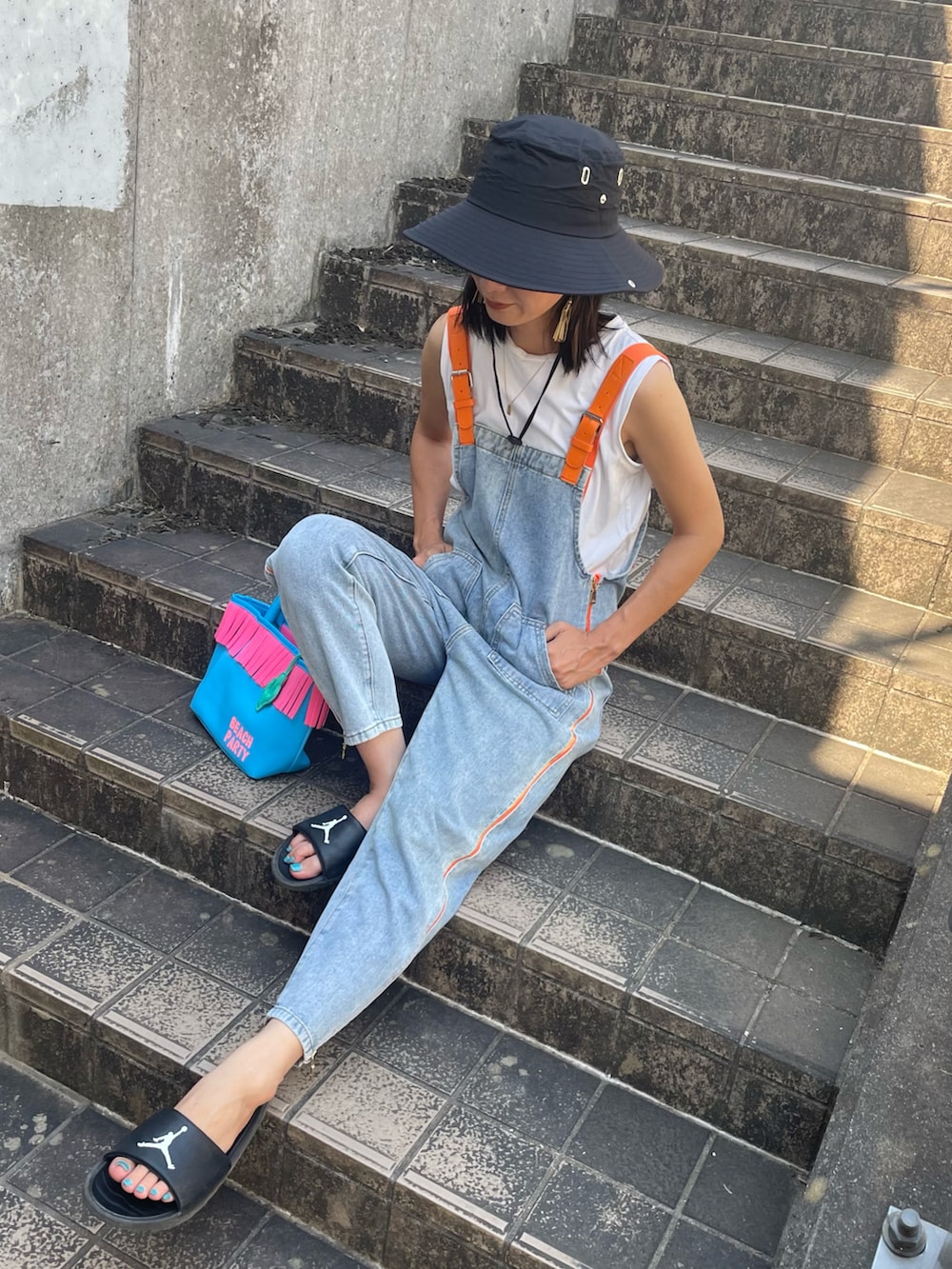 ブルー系のサロペット/オーバーオール、ホワイト系のTシャツ/カットソー、ブラック系のサンダルを着用したレディースの夏コーディネートの2枚目の写真