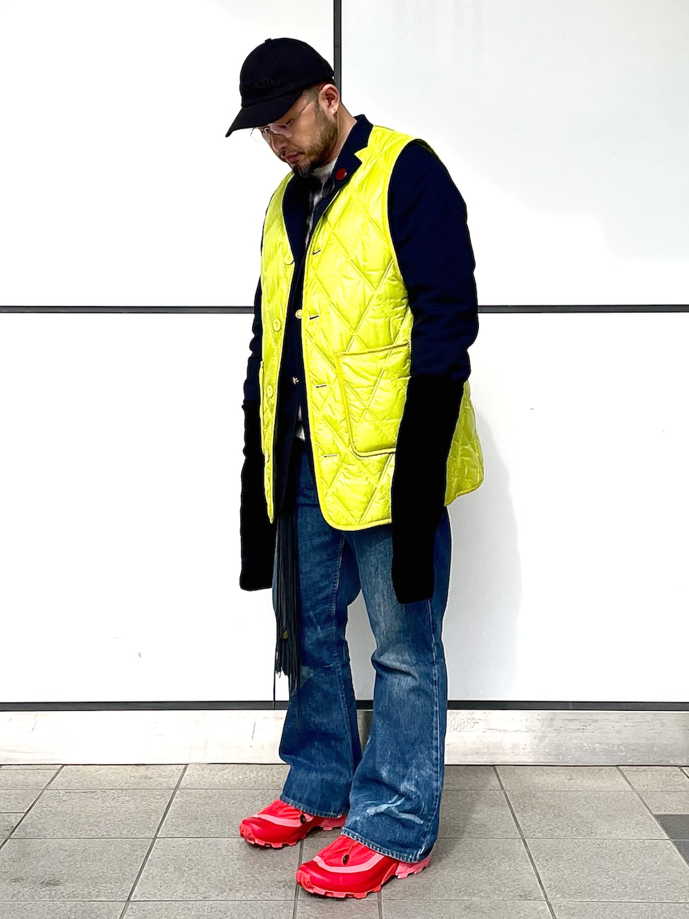 レッド系のスニーカー、ブルー系のデニムパンツ、イエロー系のベストを着用したメンズの冬コーディネートの2枚目の写真