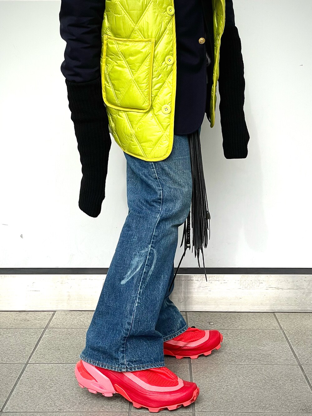 レッド系のスニーカー、ブルー系のデニムパンツ、イエロー系のベストを着用したメンズの冬コーディネートの4枚目の写真