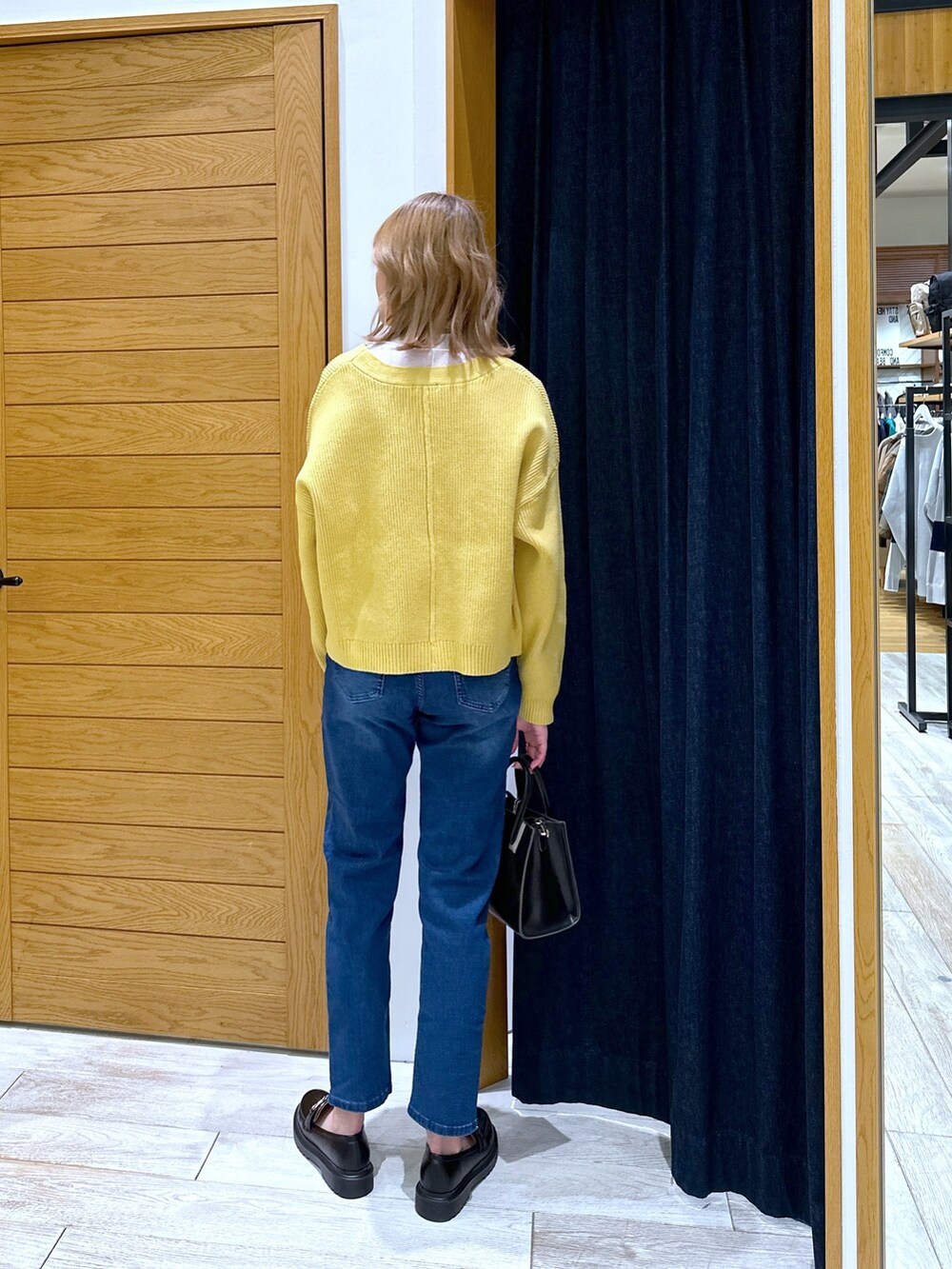 ブラック系のショルダーバッグ、ブルー系のデニムパンツ、イエロー系のカーディガン/ボレロを着用したレディースの冬コーディネートの3枚目の写真