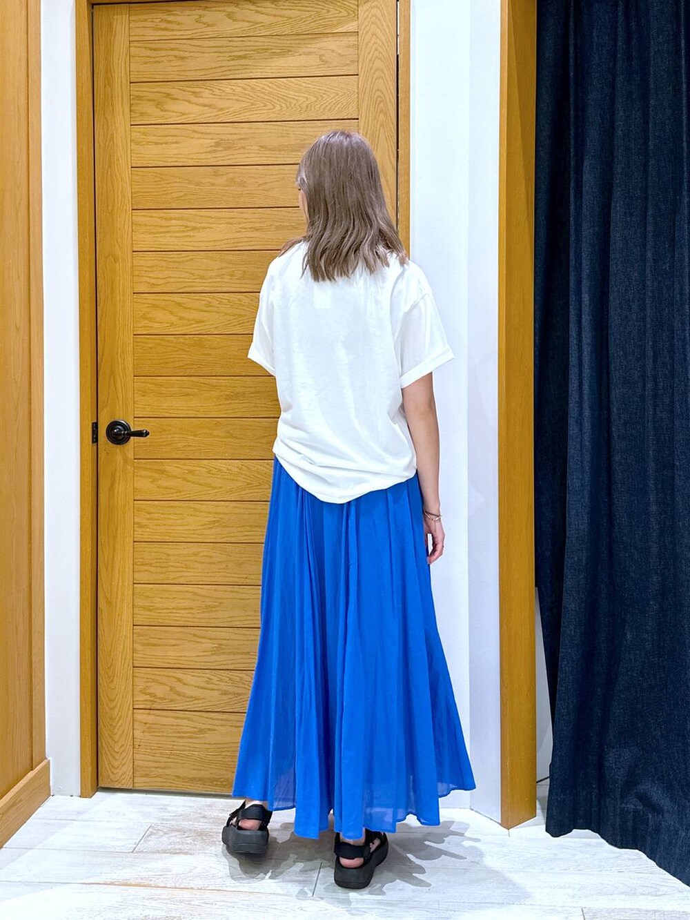 ブルー系のスカート、ブラック系のサンダル、ホワイト系のTシャツ/カットソーを着用したレディースの夏コーディネートの3枚目の写真