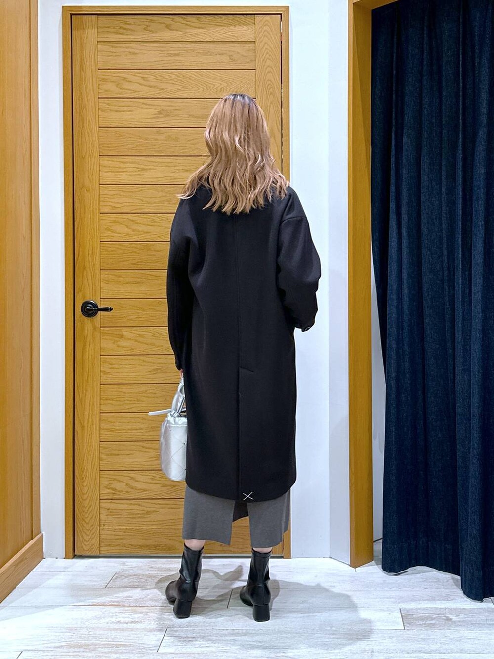 ブラック系のブーツ、ブラック系のチェスターコート、グレー系のワンピースを着用したレディースの冬コーディネートの3枚目の写真