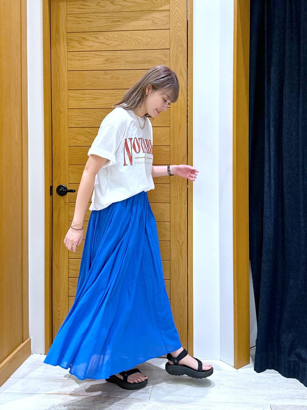 ブルー系のスカート、ブラック系のサンダル、ホワイト系のTシャツ/カットソーを着用したレディースの夏コーディネートの2枚目の写真