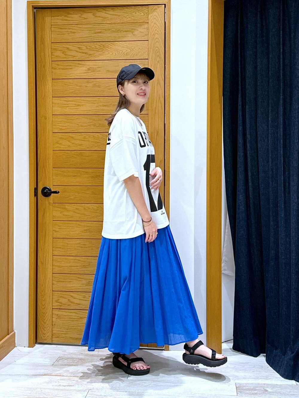 ブルー系のスカート、ブラック系のサンダル、ホワイト系のTシャツ/カットソーを着用したレディースの夏コーディネートの2枚目の写真