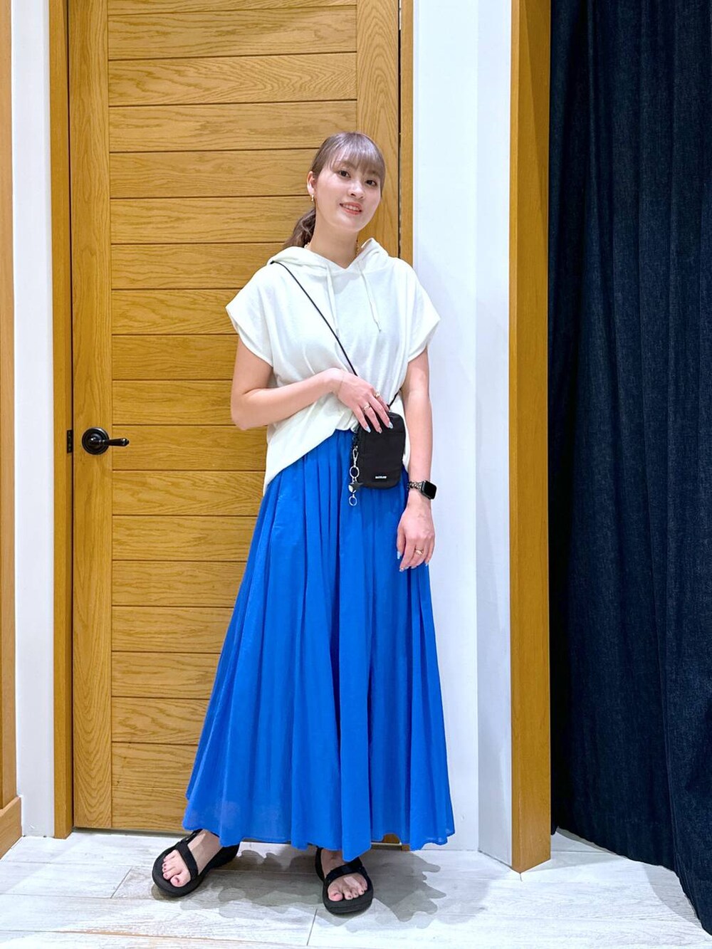 ブルー系のスカート、ホワイト系のTシャツ/カットソー、ブラック系のショルダーバッグを着用したレディースの夏コーディネートの3枚目の写真