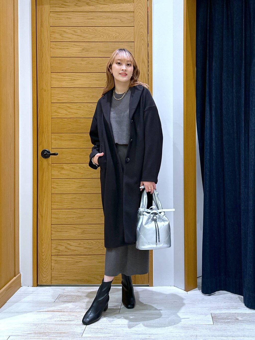 ブラック系のブーツ、ブラック系のチェスターコート、グレー系のワンピースを着用したレディースの冬コーディネートの4枚目の写真