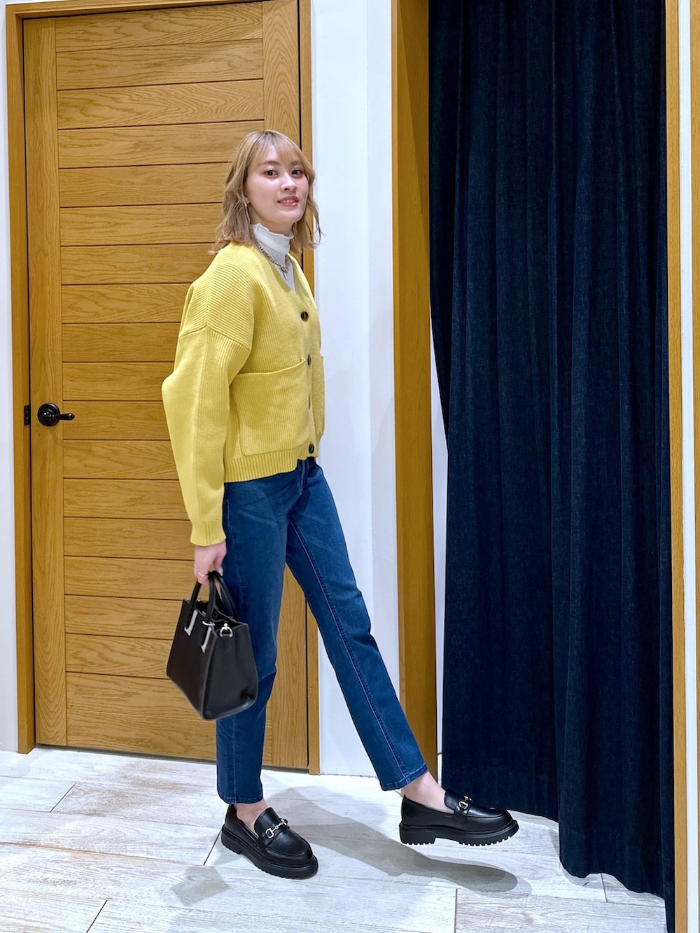 ブラック系のショルダーバッグ、ブルー系のデニムパンツ、イエロー系のカーディガン/ボレロを着用したレディースの冬コーディネートの2枚目の写真