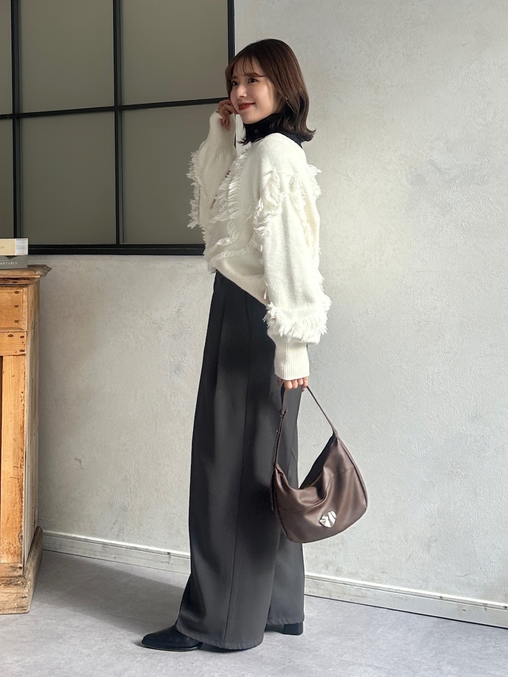 ホワイト系のニット/セーター、グレー系のスラックス、ブラック系のブーツを着用したレディースの冬コーディネートの2枚目の写真