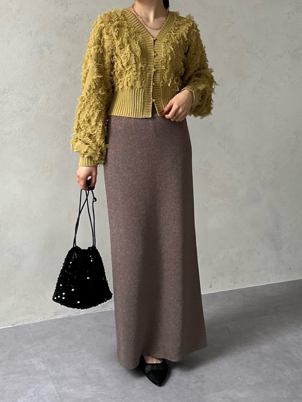 イエロー系のカーディガン/ボレロ、ブラウン系のスカート、ブラック系のパンプスを着用したレディースの冬コーディネートの3枚目の写真