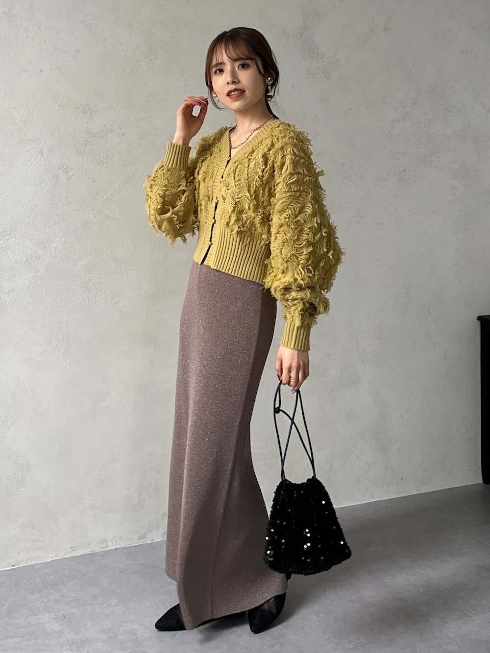 イエロー系のカーディガン/ボレロ、ブラウン系のスカート、ブラック系のパンプスを着用したレディースの冬コーディネートの4枚目の写真