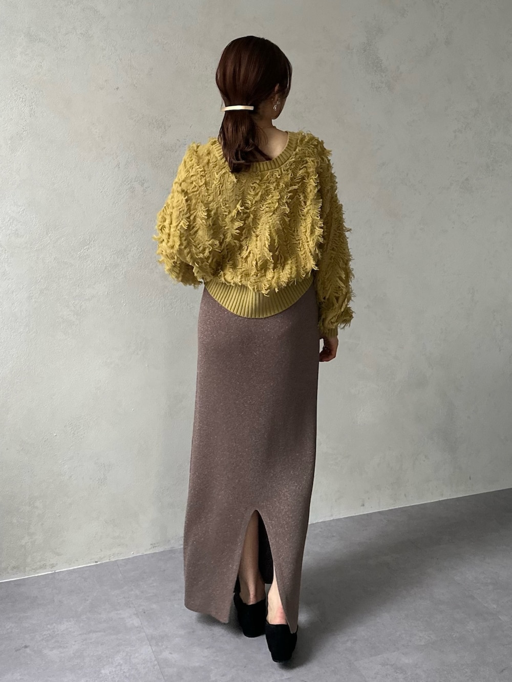 イエロー系のカーディガン/ボレロ、ブラウン系のスカート、ブラック系のパンプスを着用したレディースの冬コーディネートの2枚目の写真