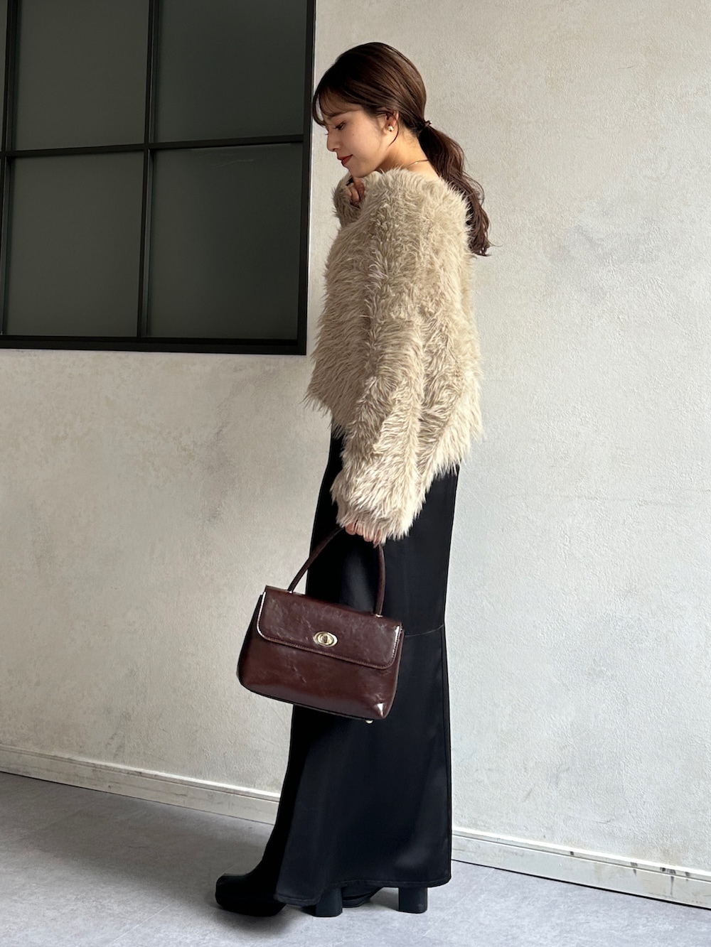 ブラック系のスカート、ブラウン系のショルダーバッグ、ブラック系のブーツを着用したレディースの冬コーディネートの3枚目の写真