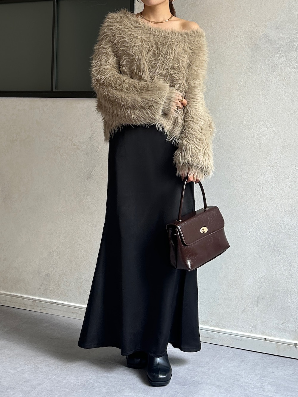 ブラック系のスカート、ブラウン系のショルダーバッグ、ブラック系のブーツを着用したレディースの冬コーディネートの2枚目の写真