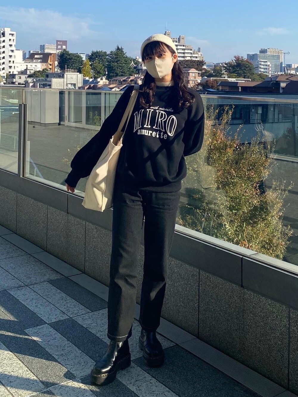 ブラック系のデニムパンツ、ブラック系のブーツ、ホワイト系のトートバッグを着用したレディースの秋コーディネートの2枚目の写真