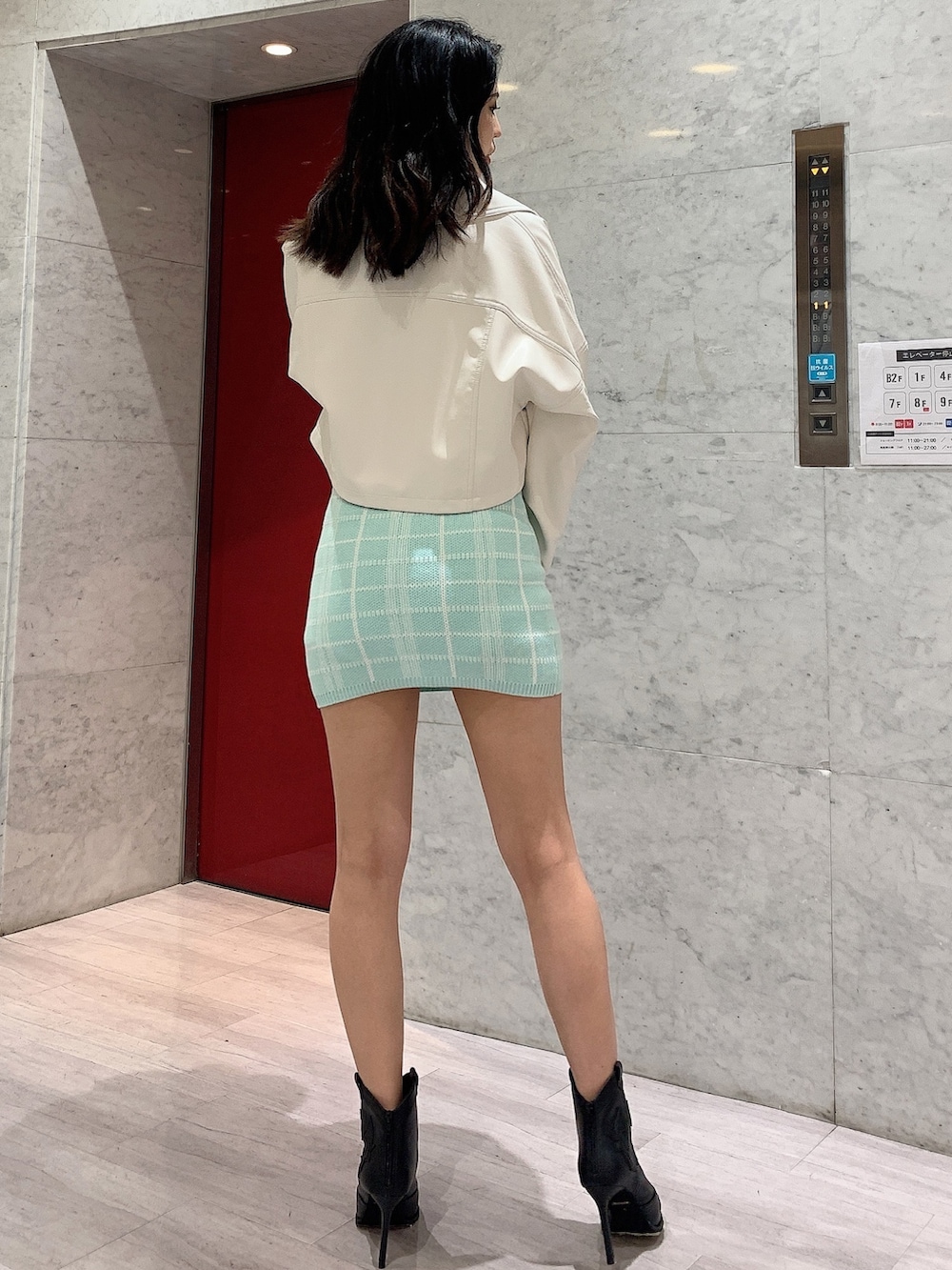 グリーン系のスカート、グリーン系のニット/セーター、ホワイト系のライダースジャケットを着用したレディースの冬コーディネートの2枚目の写真