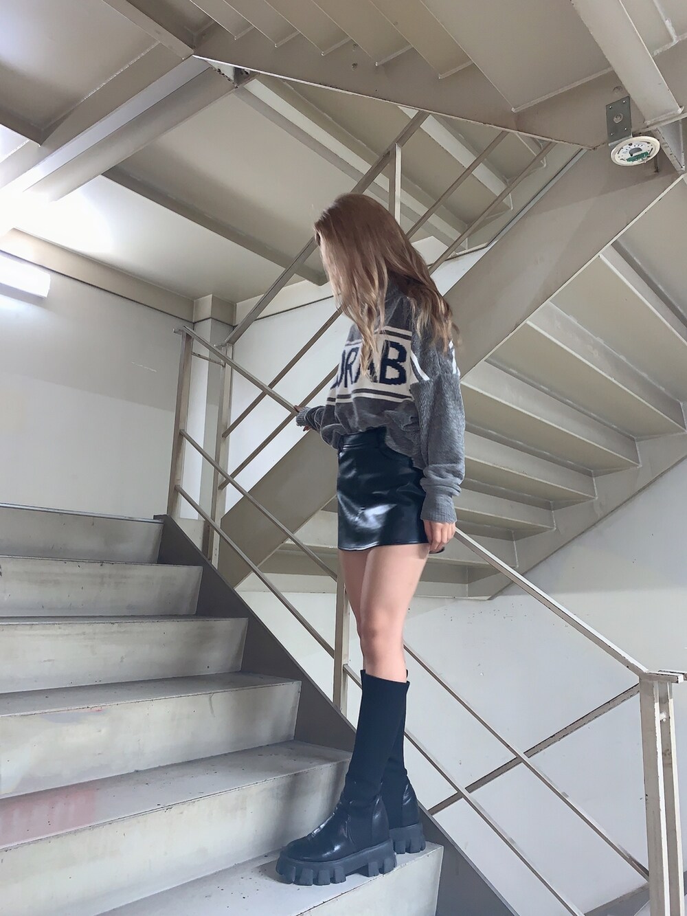 グレー系のニット/セーター、ブラック系のスカート、ブラック系のブーツを着用したレディースの秋コーディネートの4枚目の写真