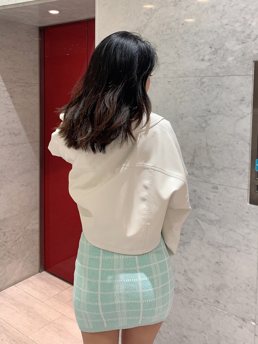 グリーン系のスカート、グリーン系のニット/セーター、ホワイト系のライダースジャケットを着用したレディースの冬コーディネートの5枚目の写真