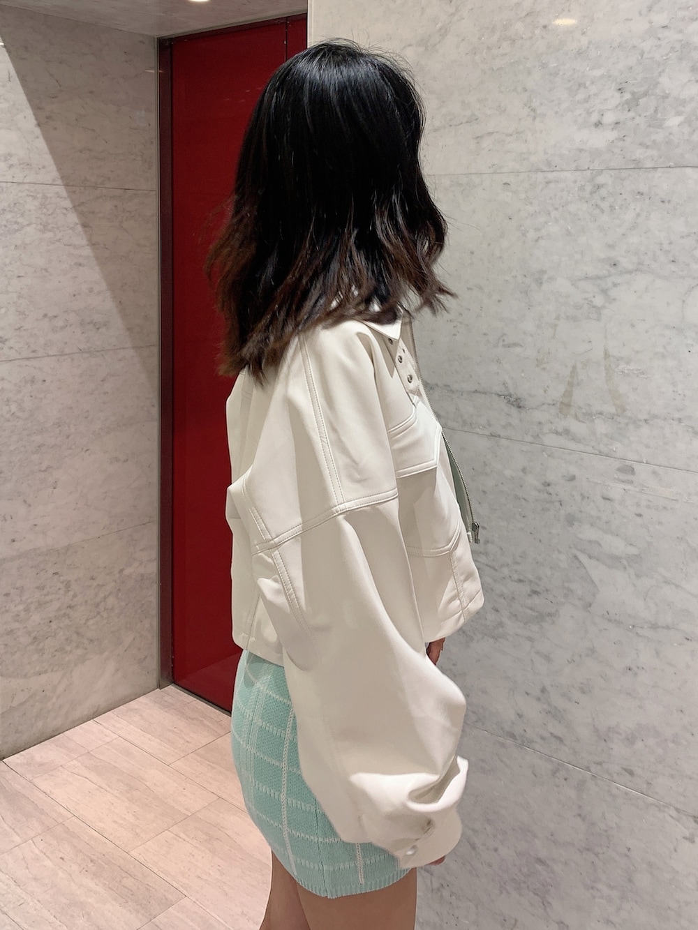 グリーン系のスカート、グリーン系のニット/セーター、ホワイト系のライダースジャケットを着用したレディースの冬コーディネートの6枚目の写真