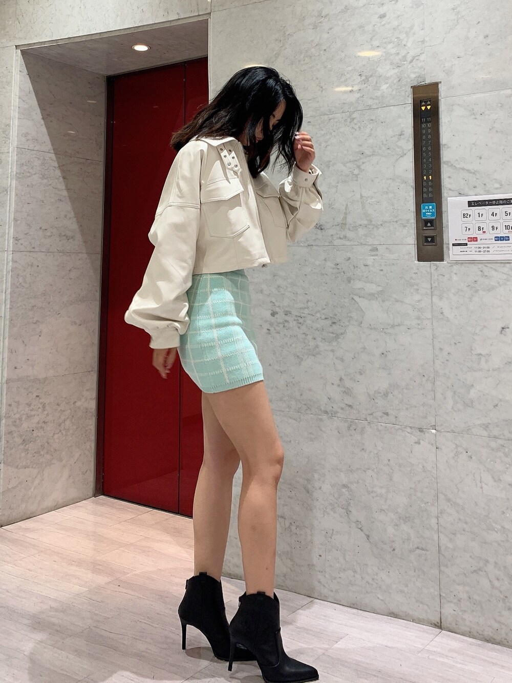 グリーン系のスカート、グリーン系のニット/セーター、ホワイト系のライダースジャケットを着用したレディースの冬コーディネートの3枚目の写真