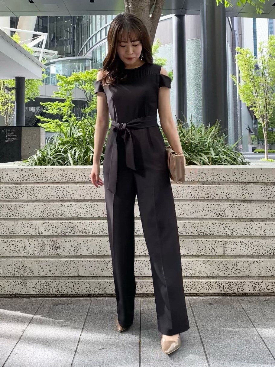 ゴールド系のハンドバッグ、ブラック系のパンツドレス、ゴールド系のパンプスを着用したレディースの春コーディネートの2枚目の写真