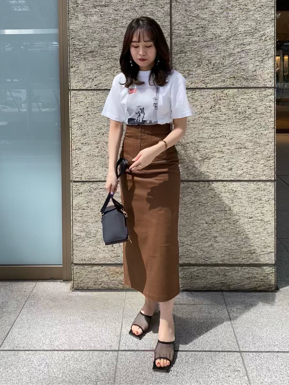 ブラウン系のスカート、ブラック系のその他シューズ、ホワイト系のTシャツ/カットソーを着用したレディースの春コーディネートの2枚目の写真