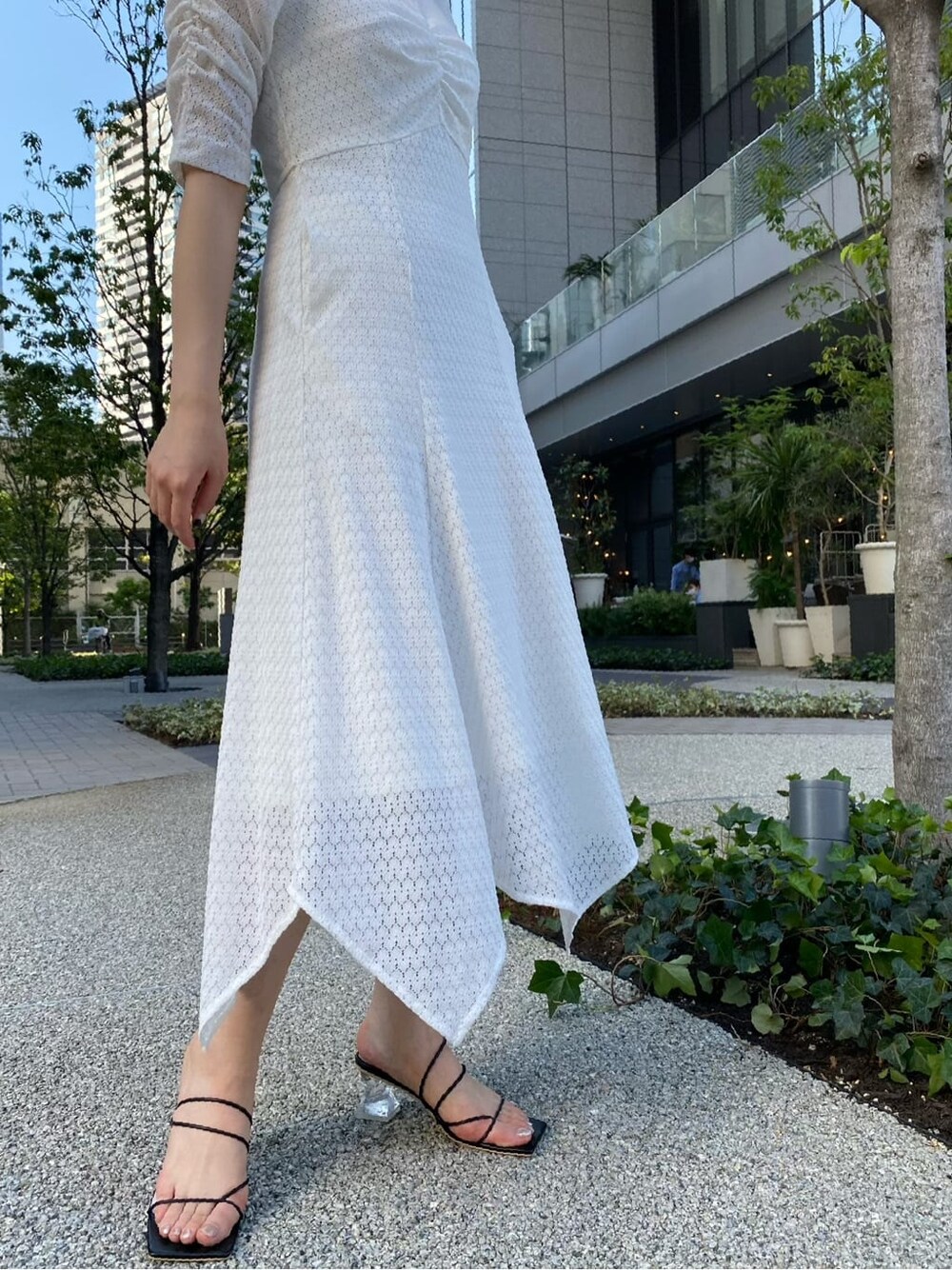 ゴールド系のハンドバッグ、ホワイト系のワンピース、ブラック系のサンダルを着用したレディースの夏コーディネートの3枚目の写真